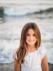 Portrait of charming little girl standing in water on beach and looking at camera — Stock Photo