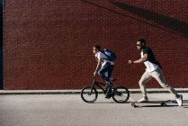 Jeunes hommes afro-américains à vélo et planche à roulettes — Photo de stock