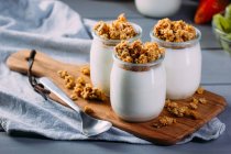 Óculos de leite saboroso frio e deliciosa granola na tábua de madeira — Fotografia de Stock