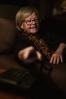 Mulher idosa atende telefonema enquanto está sentada no quarto escuro à noite em casa — Fotografia de Stock