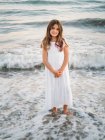 Portrait of charming little girl standing in water on beach and looking at camera — Stock Photo