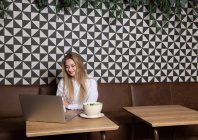 Female freelancer browsing modern laptop while sitting at table with bowl of healthy salad in cozy restaurant — Stock Photo