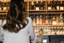 Blick von hinten auf eine anonyme Frau, die an der Bar eines gemütlichen Restaurants einen Cocktail hält — Stockfoto