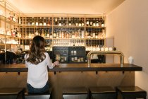 Ззаду анонімної жінки, яка тримає коктейль, сидячи в барі затишного ресторану — стокове фото