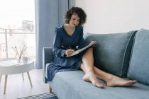 Elegante donna seduta su un divano che disegna su un taccuino a casa — Foto stock