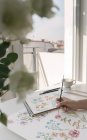 Abgeschnittene Person Hand mit Pinsel malen Aquarell Blumen auf Blatt am Schreibtisch — Stockfoto