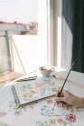 Ritagliato di persona mano con pennello pittura ad acquerello fiori su grande foglio alla scrivania — Foto stock