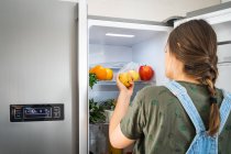 Mulher irreconhecível tomando pêra fresca da prateleira do refrigerador em casa — Fotografia de Stock
