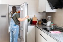 Неузнаваемая женщина берет свежие фрукты с полки холодильника дома — стоковое фото