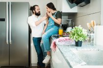 Bärtiger Mann füttert Freundin mit gesundem Essen und verbringt Zeit in der Küche zu Hause zusammen — Stockfoto