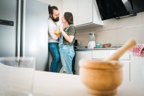Blurred wooden mortar and pestle placed on lumber tabletop of kitchen with couple standing behind drinking juice at home — Stock Photo
