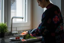 Weibchen in bunter Jacke wäscht frische Tomaten unter klarem Wasser über Spüle in der heimischen Küche — Stockfoto