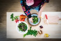 Manos de la mujer preparando verduras mientras cocina ensalada saludable en la cocina - foto de stock
