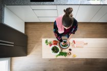 Donna in giacca multicolore preparare verdure durante la cottura di insalata sana in cucina — Foto stock