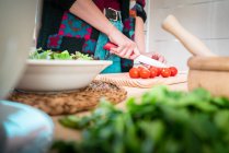 Cropped image of woman cutting tomatoes while cooking healthy salad in kitchen — Stock Photo