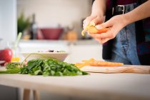 Imagem cortada de mulher cortando cenouras enquanto cozinha salada saudável na cozinha — Fotografia de Stock