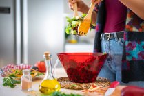 Image recadrée de la femme en veste multicolore mélangeant les légumes dans un bol tout en cuisinant une salade saine dans la cuisine — Photo de stock