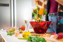 Imagen recortada de la mujer en chaqueta multicolor mezclando verduras en un tazón mientras cocina ensalada saludable en la cocina - foto de stock