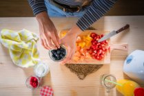Imagem cortada de mulher tomando mirtilos do frasco enquanto cozinha alimentos saudáveis de vitaminas de frutas frescas em casa — Fotografia de Stock