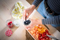 Geschnittenes Bild einer Frau, die Blaubeeren aus dem Glas nimmt, während sie zu Hause gesunde Vitaminnahrung aus frischen Früchten kocht — Stockfoto
