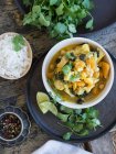 Teller mit leckerem vegetarischem Curry und Limettenscheiben auf Tablett auf Holzboden neben Reis, Pfeffer und frischen Limetten platziert — Stockfoto