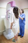 Mujer en uniforme profesional utilizando la unidad de mamografía digital mientras que el diagnóstico médico de paciente sin rostro en la clínica - foto de stock