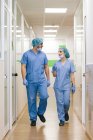 Compañeros cirujanos hombre y mujer chatear mientras camina hacia el quirófano - foto de stock