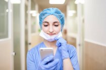 Женщина-хирург, стоящая в коридоре, проверяя сообщения на смартфоне — стоковое фото
