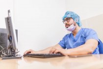 Cirujano masculino usando su computadora en su consultorio antes de la cirugía - foto de stock