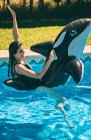 Excited young woman having fun in pool with inflatable fish toy in sunny day. — Stock Photo