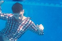 Homem de camisa posando com os olhos fechados debaixo d 'água na piscina. — Fotografia de Stock