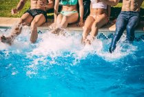 Amis assis sur le bord de la piscine et éclaboussures avec leurs pieds — Photo de stock