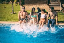Friends sitting on poolside and splashing with their feet — Stock Photo
