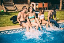 Friends sitting on poolside and splashing with their feet — Stock Photo