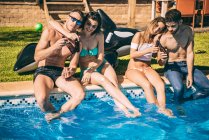Jóvenes amigos tomando bebidas en la piscina - foto de stock