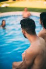 Amigos sentados na borda da piscina — Fotografia de Stock