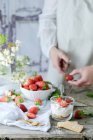 Creamy sweet dessert with fresh juicy strawberries served in glass on rustic wooden table with biscuits and female hands cutting berries on background — Stock Photo