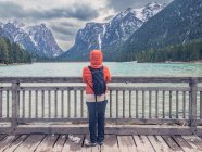 Unrecognizable tourist in warm clothes standing on wooden pier and looking at mountain ridge and rippling lake water on cloudy day in countryside — Stock Photo