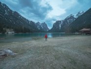 Вид ззаду дорослих мандрівників фотографує гірський хребет, стоячи на березі спокійного озера в природі — стокове фото