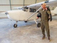 Confident pilot standing next to retro plane in hangar — Stock Photo