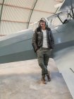 Fiducioso pilota con auricolare appoggiato su aereo retrò in hangar — Foto stock