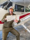 Konzentrierter männlicher Pilot in Ausrüstung, die neben Flugzeug steht und Landkarte studiert — Stockfoto