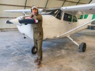 Portrait of confident pilot standing near retro plane in hangar — Stock Photo