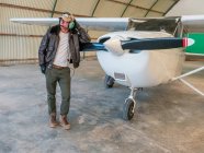 Selbstbewusster Pilot lehnt an Retro-Flugzeug im Hangar — Stockfoto