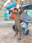Confident pilot in helmet standing near retro plane in hangar — Stock Photo