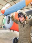 Selbstbewusster Pilot mit Helm steht neben Retro-Flugzeug im Hangar — Stockfoto