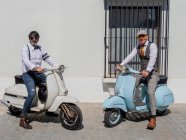 Hipsters positivos de mediana edad en ropa elegante con motos retro mirando a la cámara en un día soleado - foto de stock