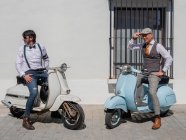Hipsters positivos de meia-idade em roupas elegantes com motos retro olhando para longe em dia ensolarado — Fotografia de Stock