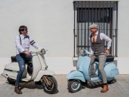 Hipsters positivos de mediana edad en ropa elegante con motos retro mirándose en un día soleado - foto de stock