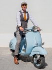 Hipster positivo de mediana edad en ropa elegante con moto retro mirando hacia otro lado en un día soleado - foto de stock